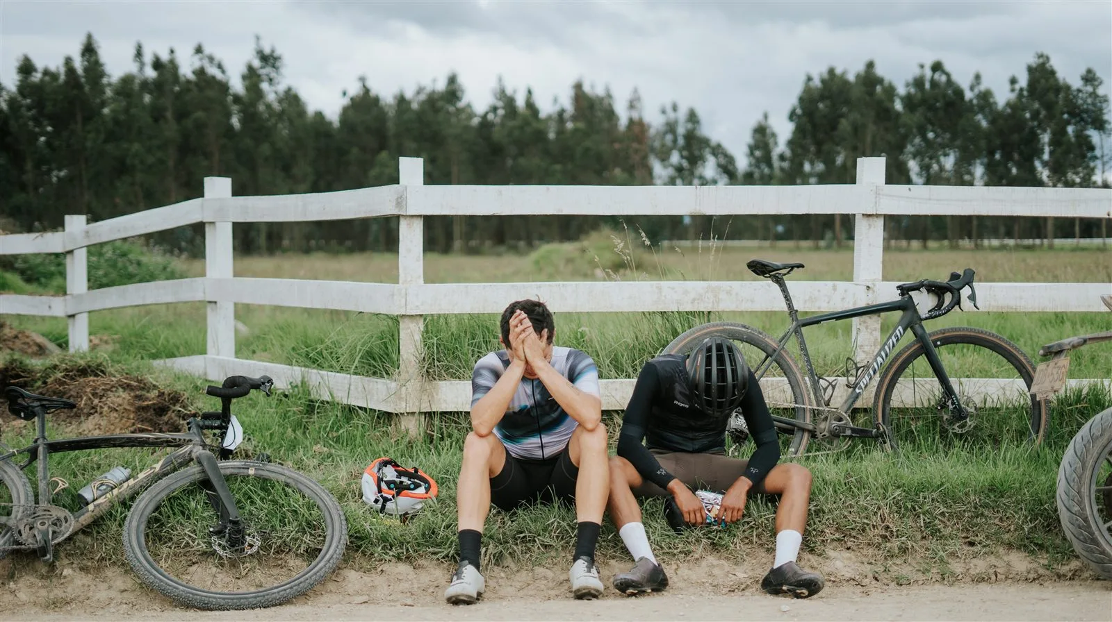 Dos ciclistas agotados descansando junto a sus bicicletas de gravel al borde de la ruta, después de una rodada de Rural Cycle
